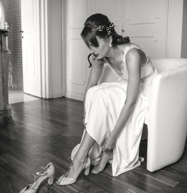Sposa in preparazione in una suite elegante, mentre si veste davanti allo specchio in un’atmosfera intima e luminosa.